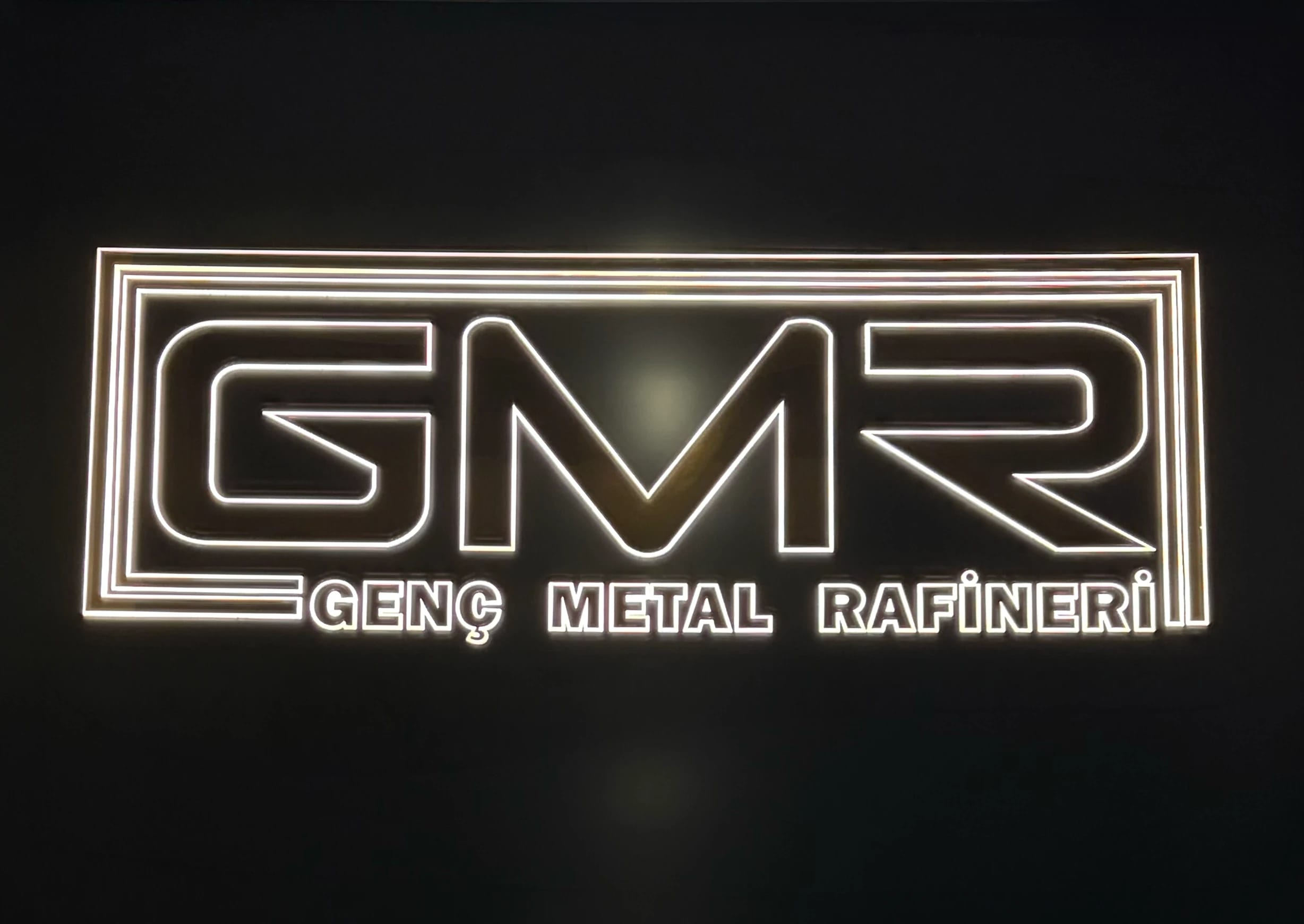 Siyah zeminde ışıklı GMR Genç Metal Rafineri tabelası